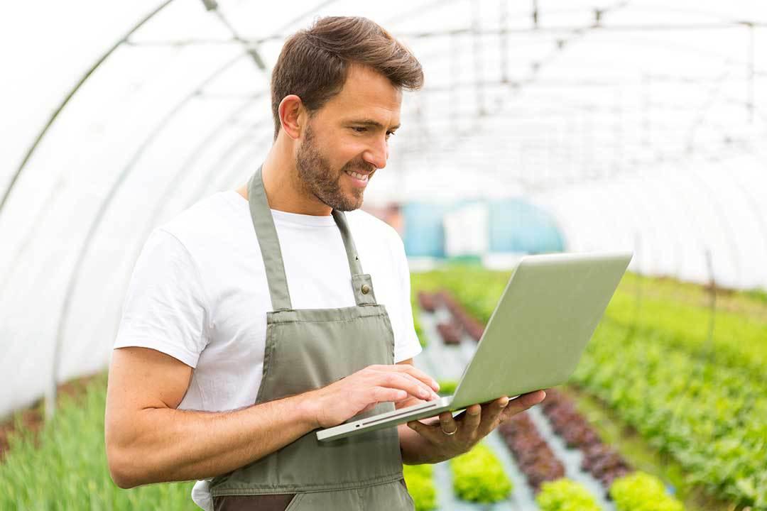 Man with a laptop smiling in a polytunnel.